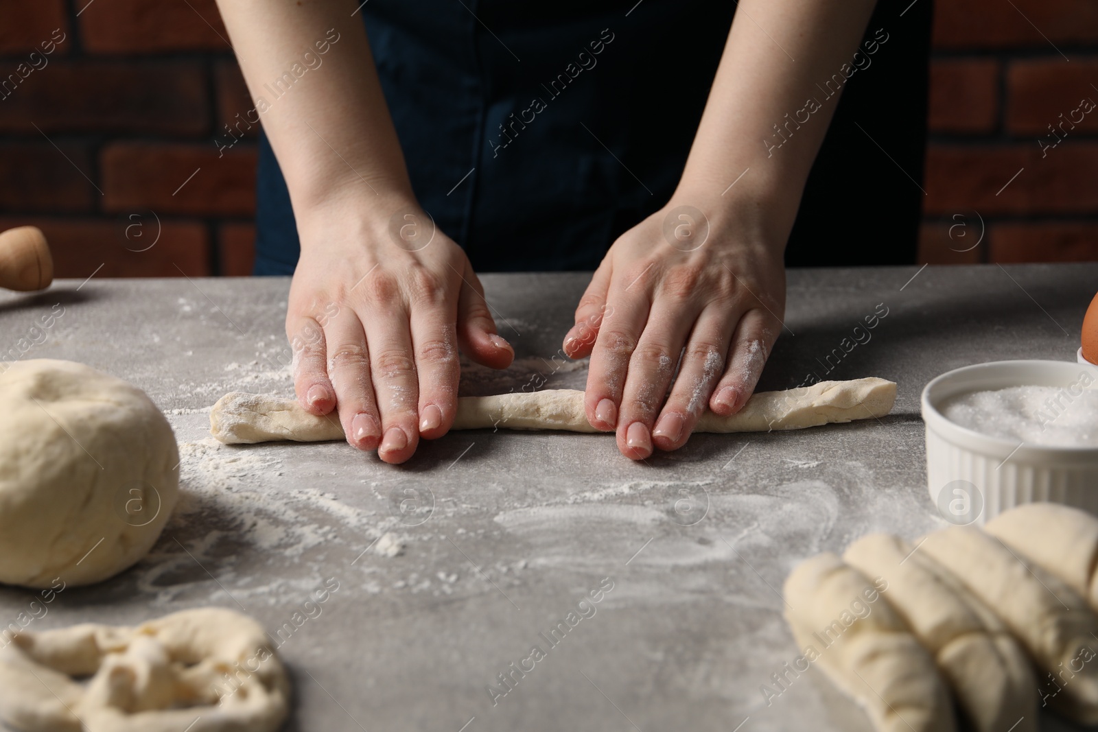 Woman making pretzel at light grey table, closeup Photo of Woman making pretzel at light grey table, closeup