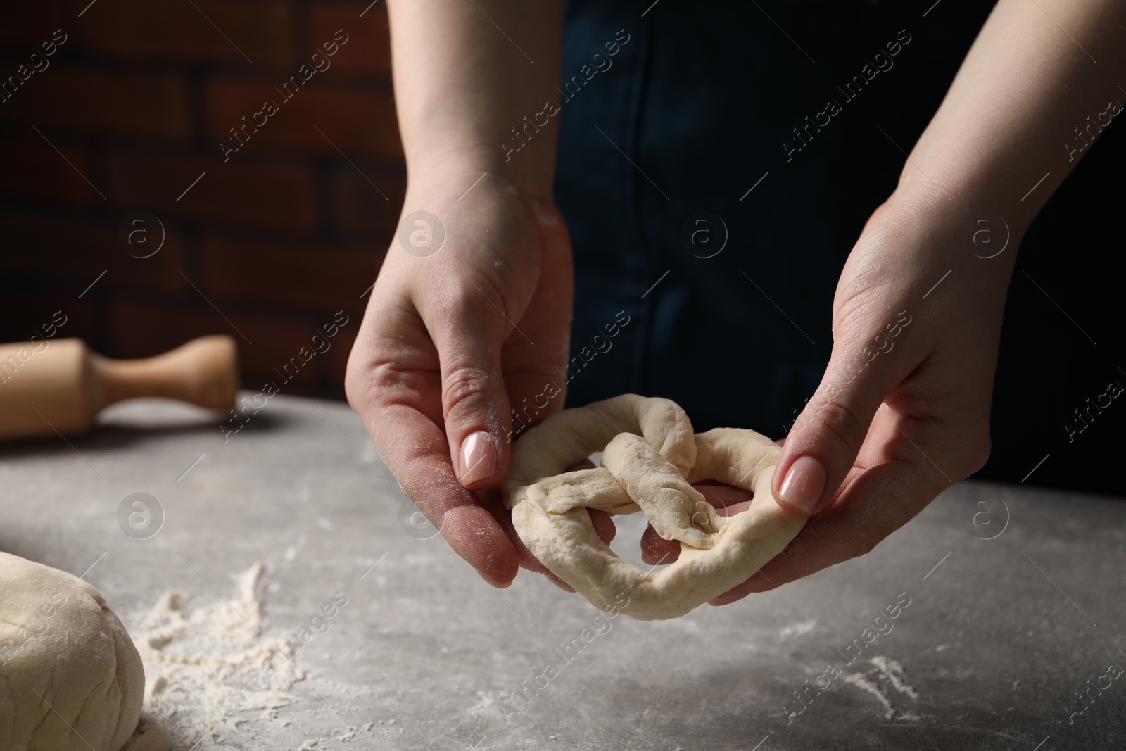 Woman making pretzel at light grey table, closeup Photo of Woman making pretzel at light grey table, closeup