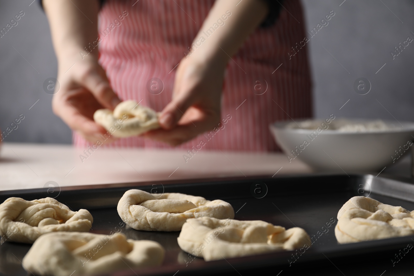 Woman putting salt onto raw pretzels at white table, closeup Photo of Woman putting salt onto raw pretzels at white table, closeup