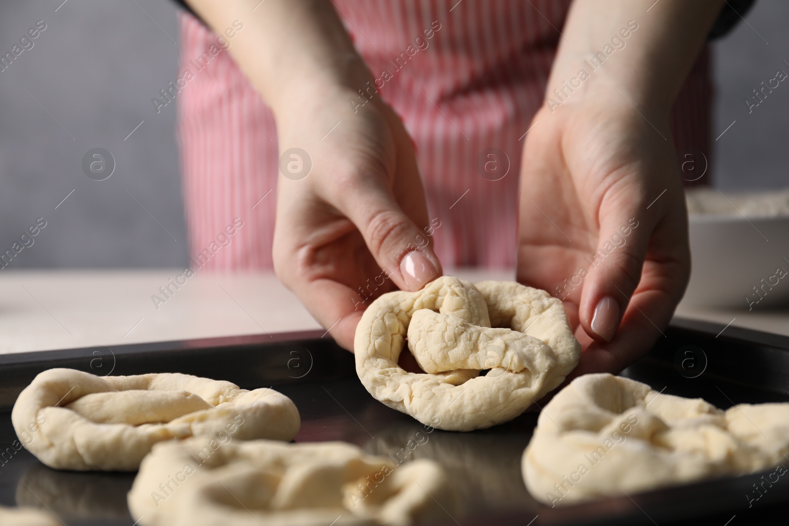 Photo of Woman putting salt onto raw pretzels at white table, closeup