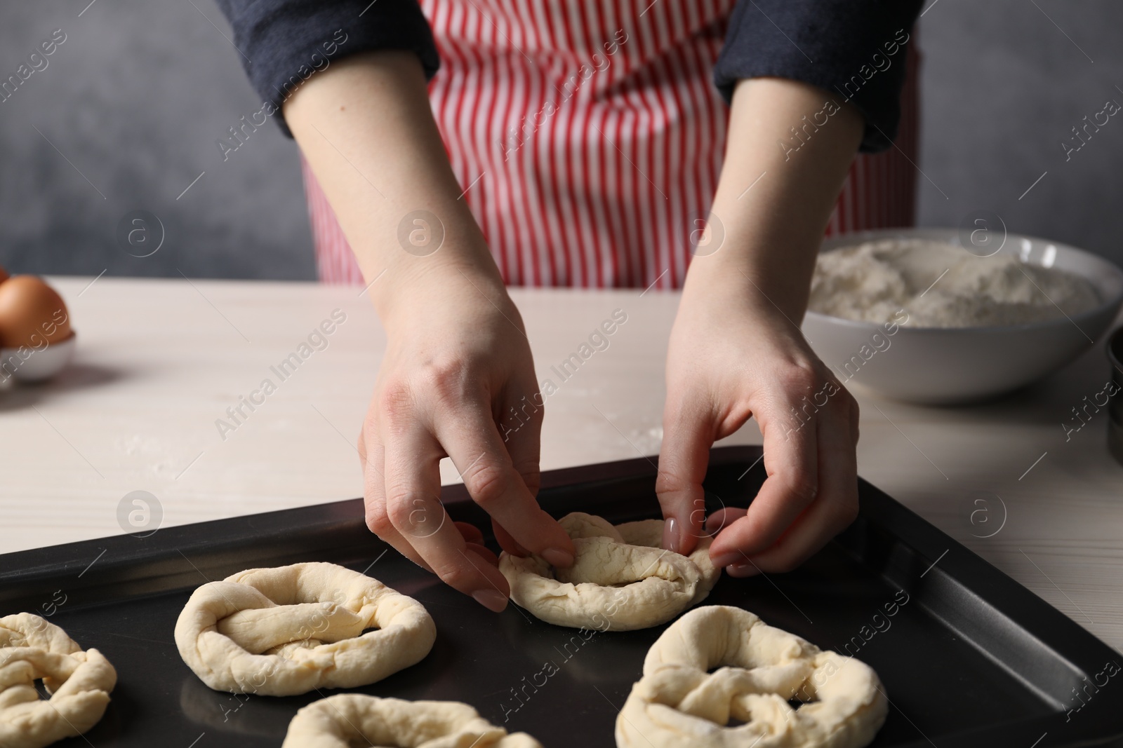 Woman putting salt onto raw pretzels at white wooden table, closeup Photo of Woman putting salt onto raw pretzels at white wooden table, closeup