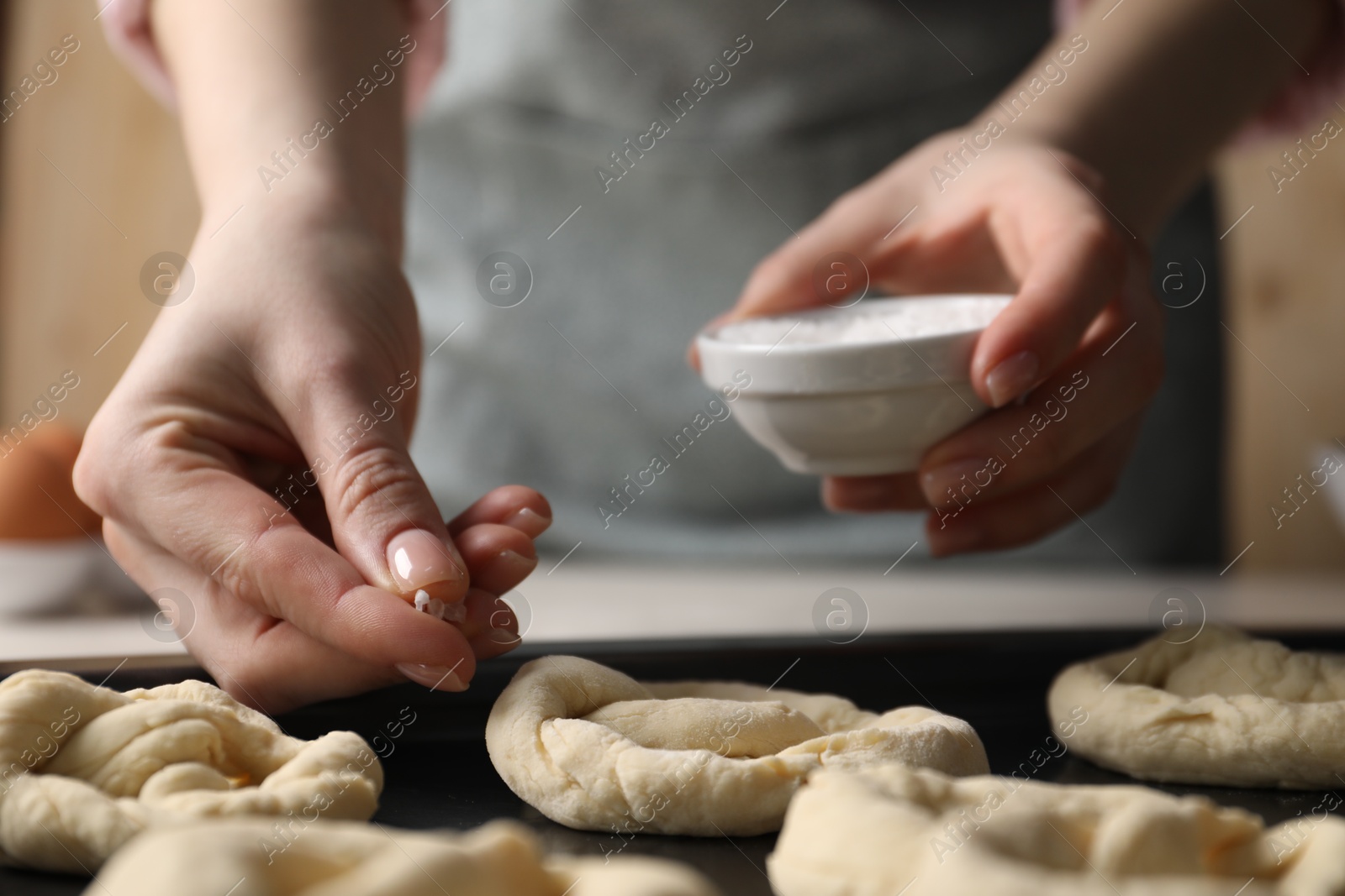 Woman putting salt onto raw pretzels at white table, closeup Photo of Woman putting salt onto raw pretzels at white table, closeup