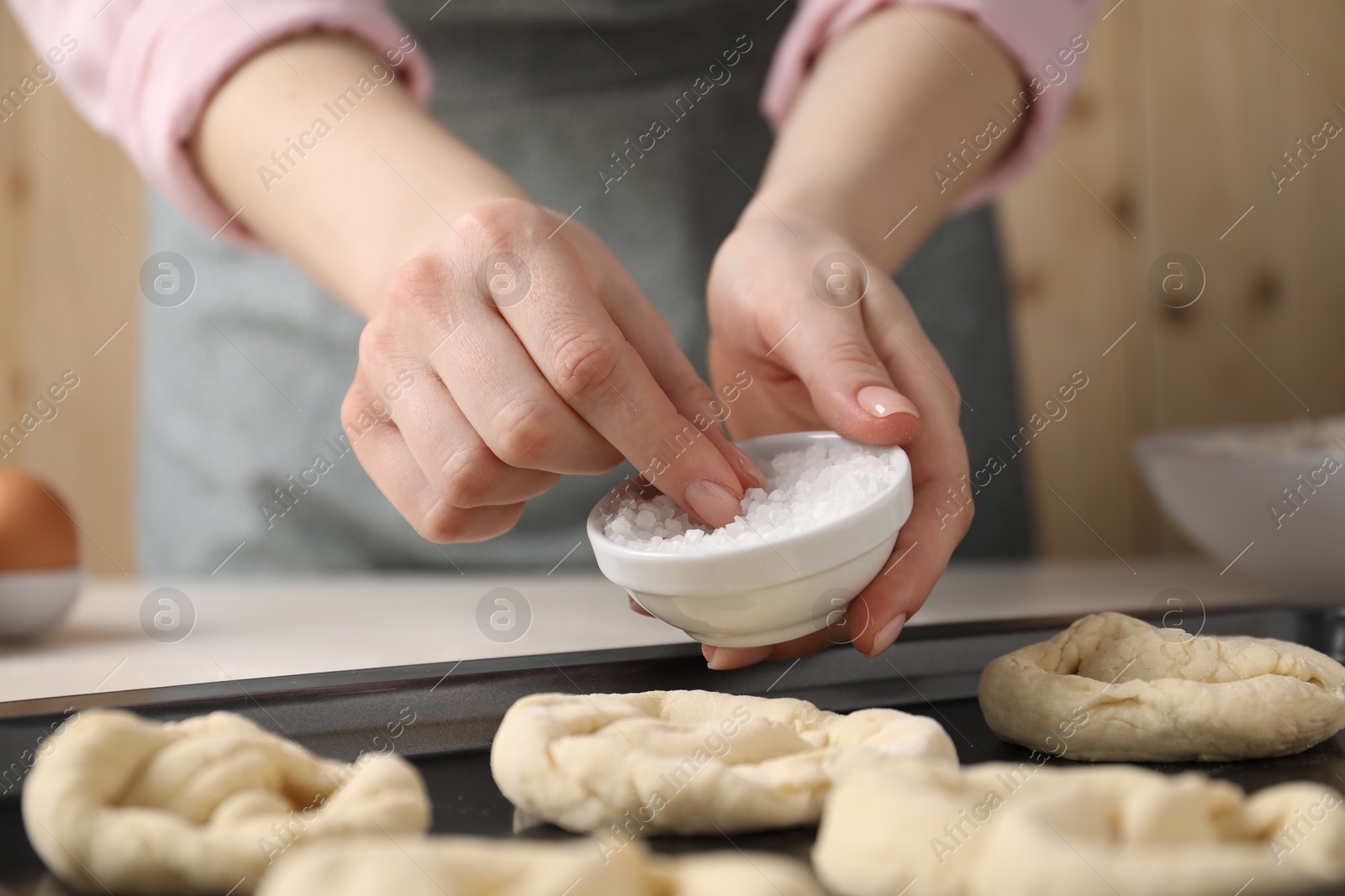 Woman putting salt onto raw pretzels at white table, closeup Photo of Woman putting salt onto raw pretzels at white table, closeup