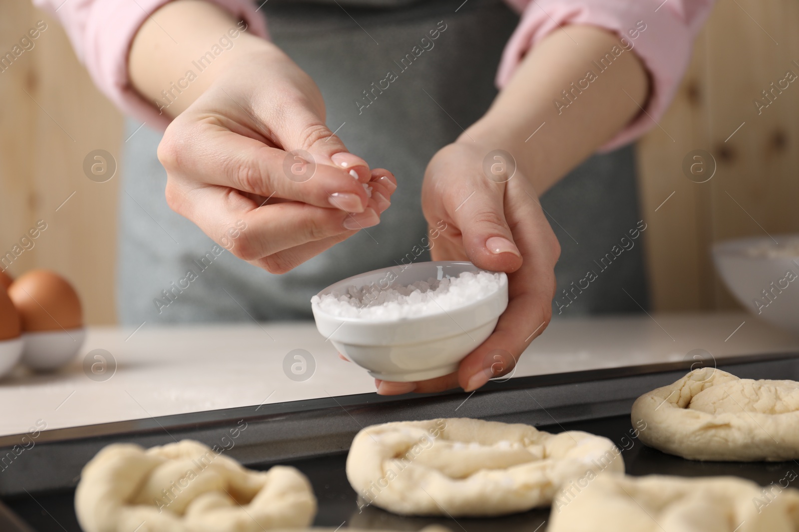 Photo of Woman putting salt onto raw pretzels at white table, closeup