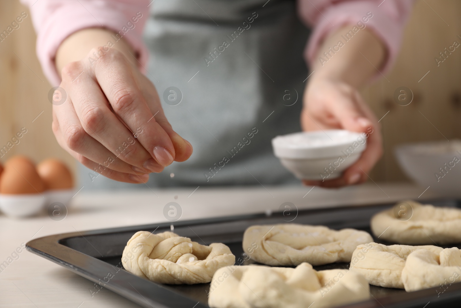 Woman putting salt onto raw pretzels at white wooden table, closeup Photo of Woman putting salt onto raw pretzels at white wooden table, closeup