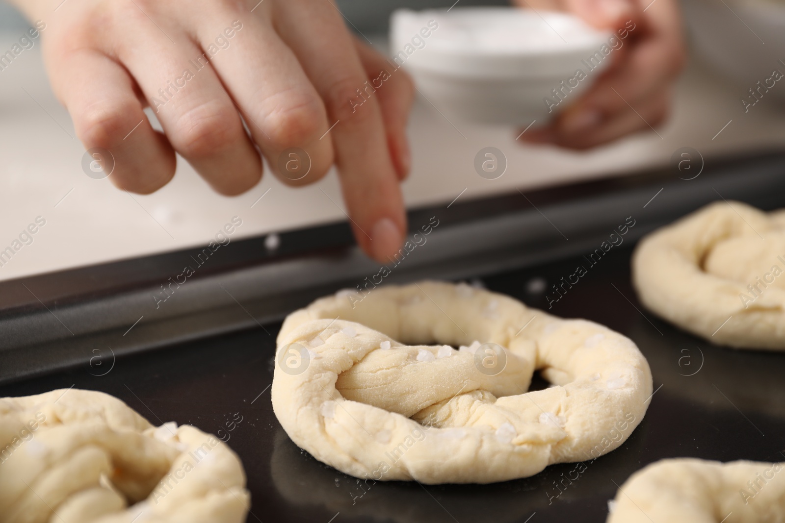 Woman putting salt onto raw pretzels at white table, closeup Photo of Woman putting salt onto raw pretzels at white table, closeup