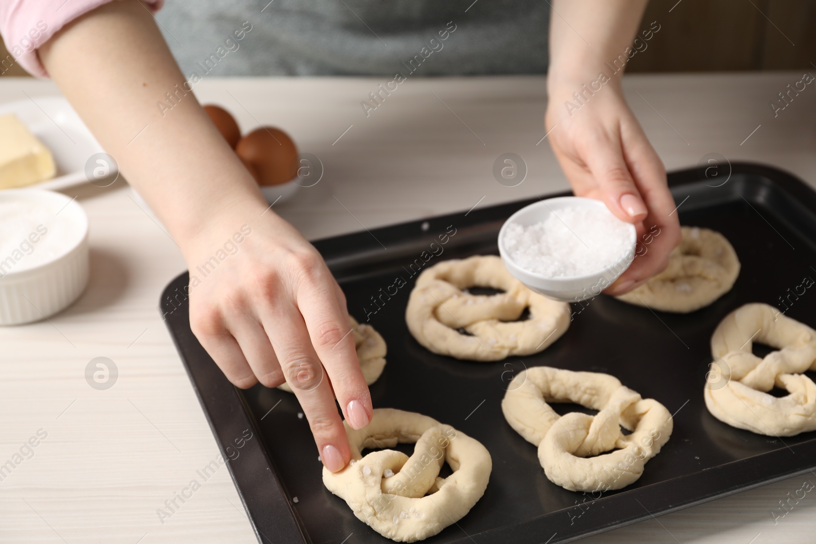 Woman putting salt onto raw pretzels at white wooden table, closeup Photo of Woman putting salt onto raw pretzels at white wooden table, closeup