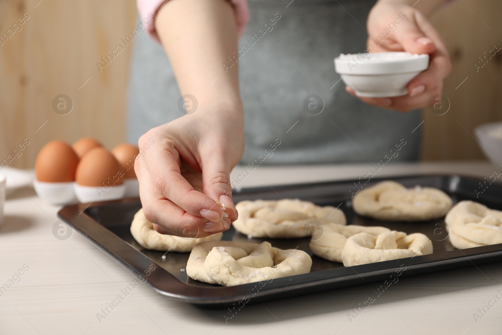 Woman putting salt onto raw pretzels at white wooden table, closeup Photo of Woman putting salt onto raw pretzels at white wooden table, closeup