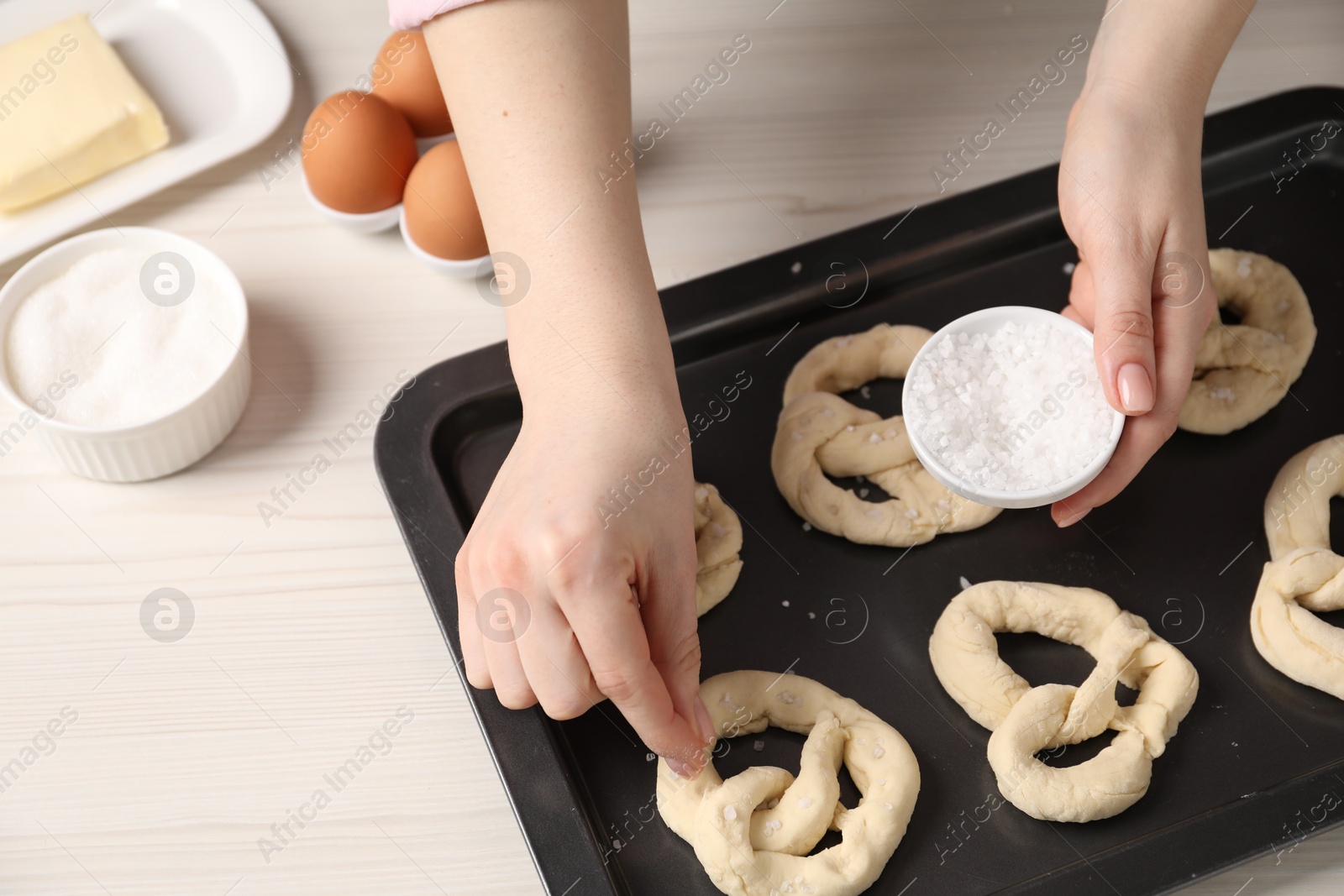 Woman putting salt onto raw pretzels at white wooden table, closeup Photo of Woman putting salt onto raw pretzels at white wooden table, closeup