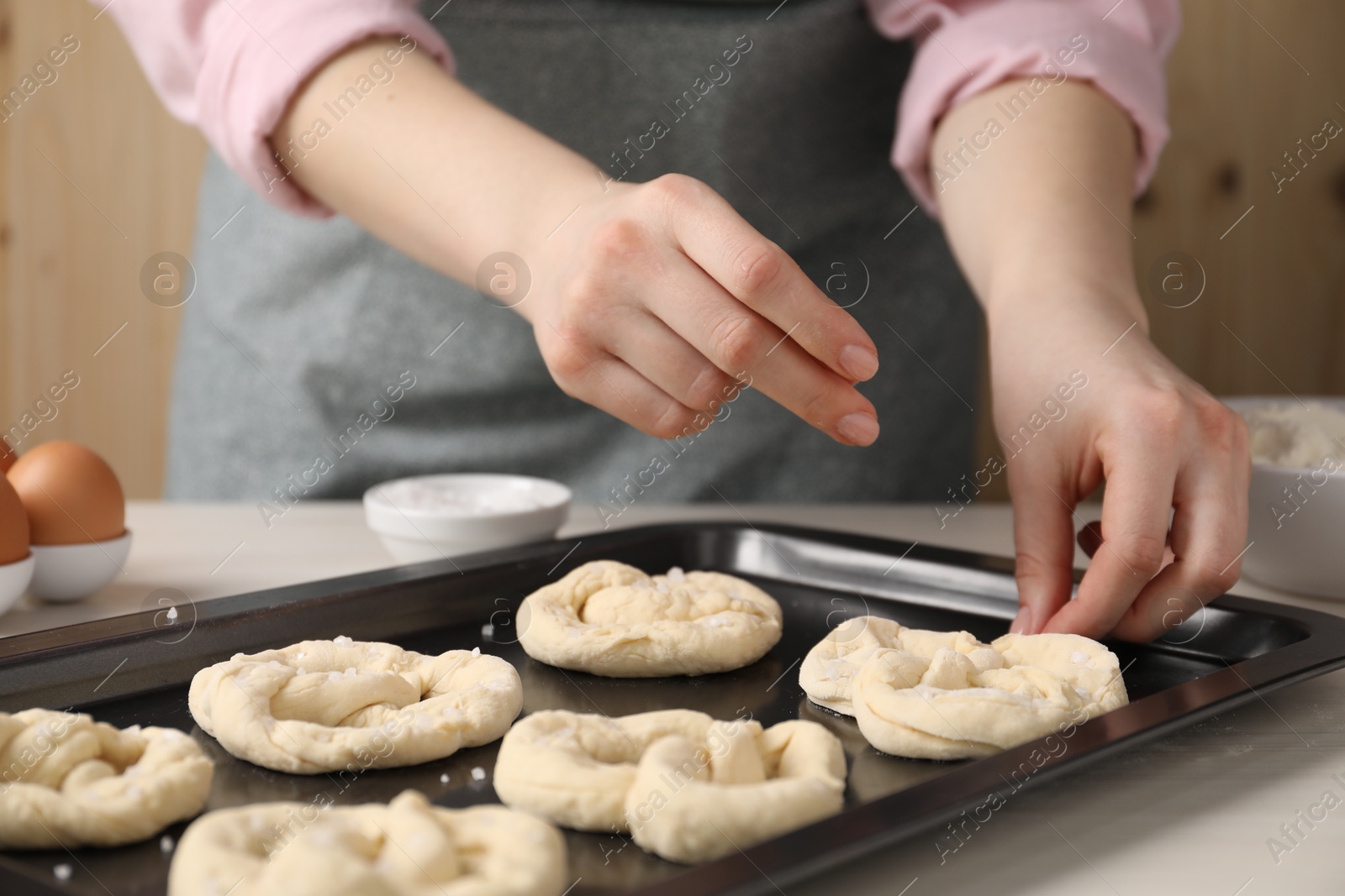 Woman putting salt onto raw pretzels at white wooden table, closeup Photo of Woman putting salt onto raw pretzels at white wooden table, closeup