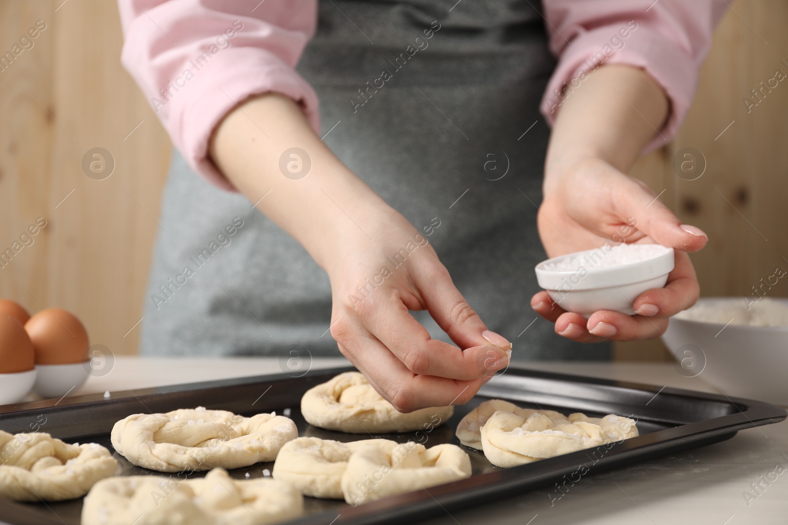 Woman putting salt onto raw pretzels at white wooden table, closeup Photo of Woman putting salt onto raw pretzels at white wooden table, closeup