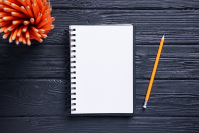 Photo of Open blank notebook and pencils on black wooden table, flat lay