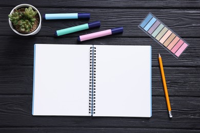 Photo of Open blank notebook, houseplant, pencil, markers and bookmarks on black wooden table, flat lay