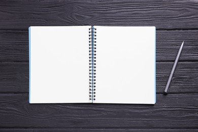 Photo of Open blank notebook and pencil on black wooden table, top view