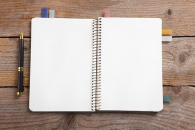 Photo of Open blank notebook with bookmarks and pen on wooden table, top view