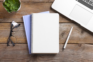Photo of Blank notebooks, laptop, houseplant, glasses and pen on wooden table, flat lay