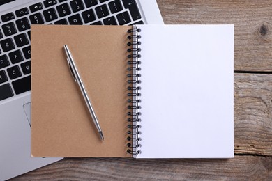 Photo of Open blank notebook, laptop and pen on wooden table, flat lay