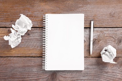 Photo of Open blank notebook, crumpled paper and pen on wooden table, flat lay