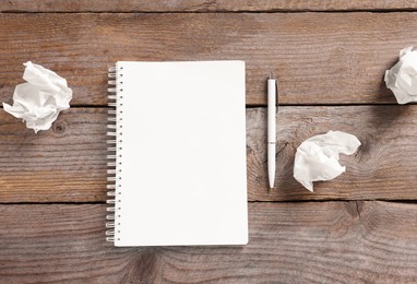 Photo of Open blank notebook, crumpled paper and pen on wooden table, flat lay