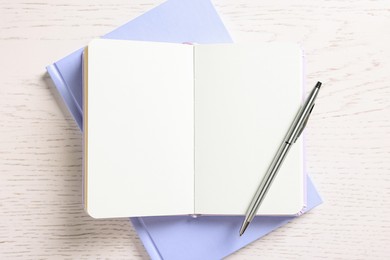 Photo of Blank notebooks and pen on white wooden table, top view
