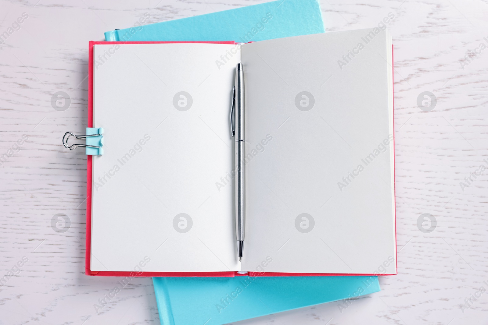 Blank notebooks, binder clip and pen on white wooden table, top view Photo of Blank notebooks, binder clip and pen on white wooden table, top view