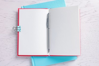 Photo of Blank notebooks, binder clip and pen on white wooden table, top view