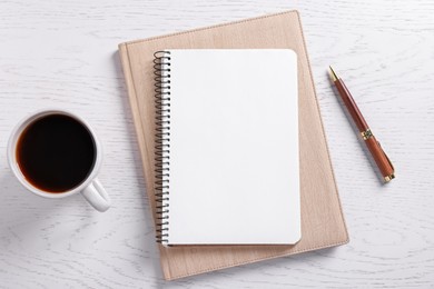 Photo of Blank notebooks, coffee and pen on white wooden table, flat lay