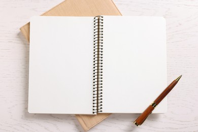 Photo of Blank notebooks and pen on white wooden table, top view