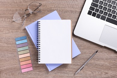 Photo of Blank notebooks, laptop, glasses and stationery on wooden table, flat lay