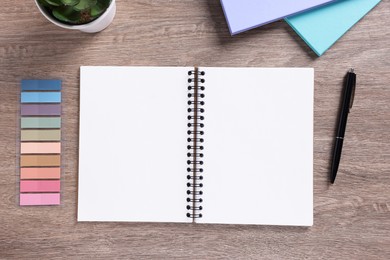 Photo of Open blank notebook, houseplant and stationery on wooden table, flat lay