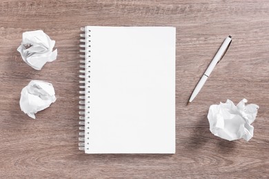 Photo of Open blank notebook, crumpled paper and pen on wooden table, flat lay