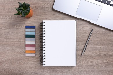 Photo of Open blank notebook, houseplant, laptop and stationery on wooden table, flat lay