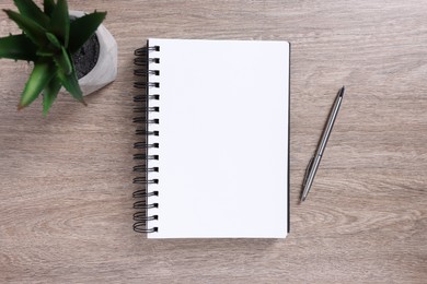 Photo of Open blank notebook, houseplant and pen on wooden table, flat lay