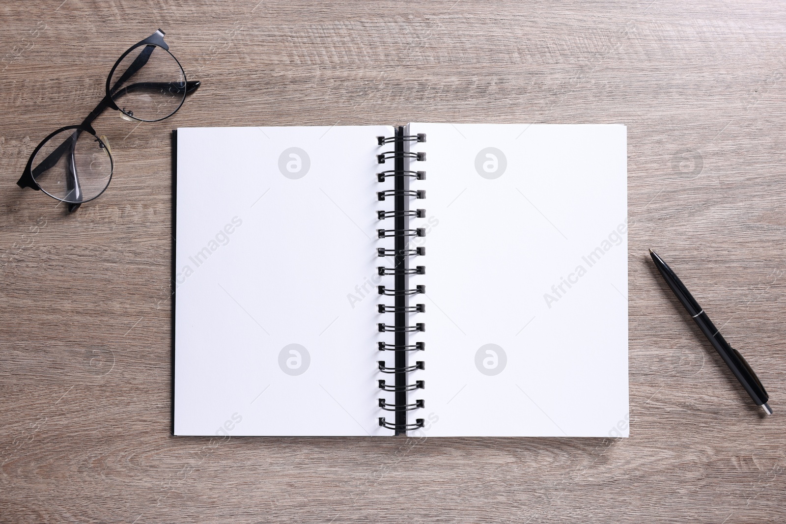 Photo of Open blank notebook, glasses and pen on wooden table, flat lay