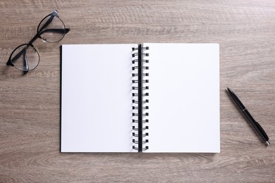 Photo of Open blank notebook, glasses and pen on wooden table, flat lay
