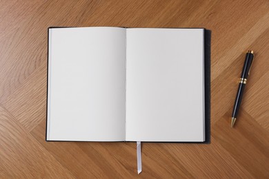 Photo of Open blank notebook and pen on wooden table, top view