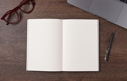 Photo of Open blank notebook, laptop, pen and glasses on wooden table, flat lay