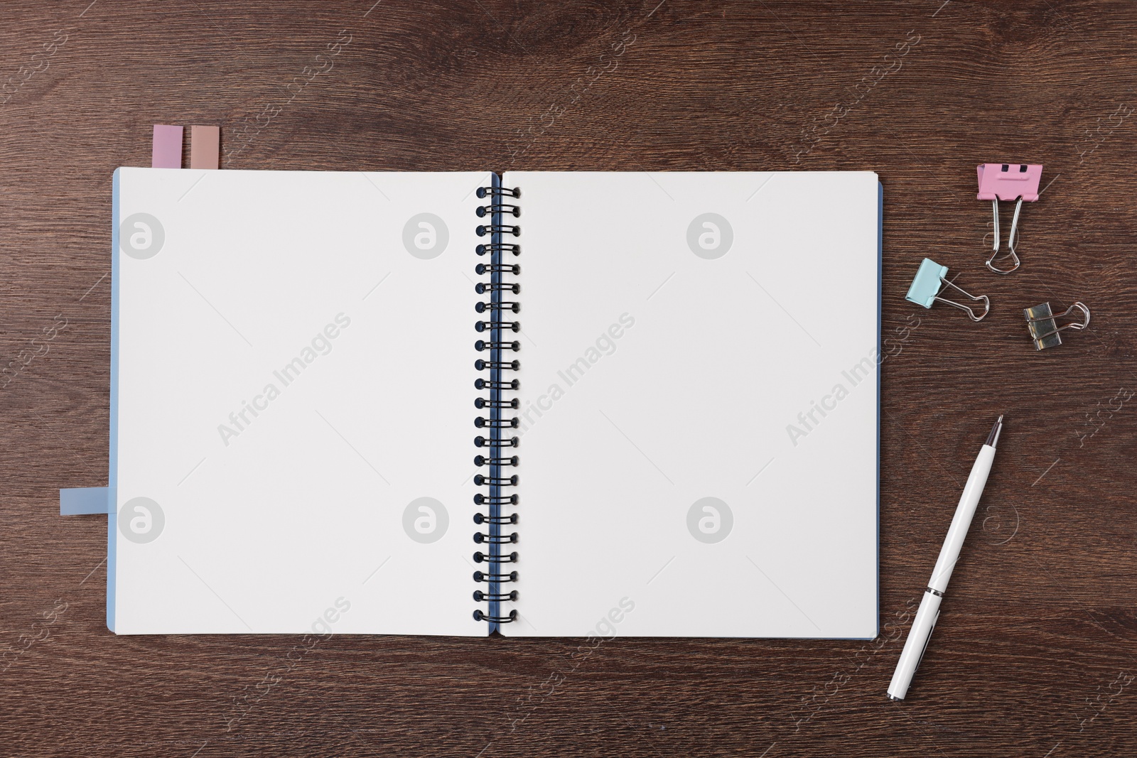 Open blank notebook with bookmarks, pen and binder clips on wooden table, flat lay Photo of Open blank notebook with bookmarks, pen and binder clips on wooden table, flat lay