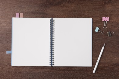 Photo of Open blank notebook with bookmarks, pen and binder clips on wooden table, flat lay