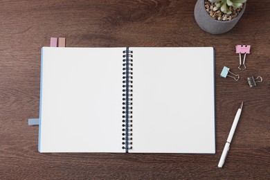 Photo of Open blank notebook, stationery and houseplant on wooden table, flat lay