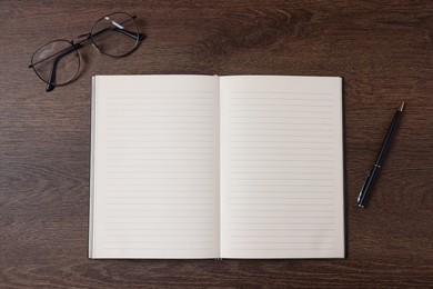 Photo of Open blank notebook, pen and glasses on wooden table, flat lay