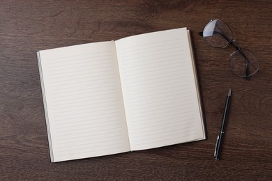 Photo of Open blank notebook, pen and glasses on wooden table, flat lay