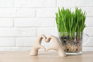 Photo of Wheat grass in transparent pot and decor on wooden table near white brick wall. Space for text