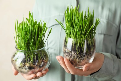 Photo of Woman with wheat grass in transparent pot on light background, closeup