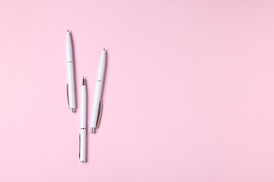 Photo of Ballpoint pens on pink background, flat lay. Space for text