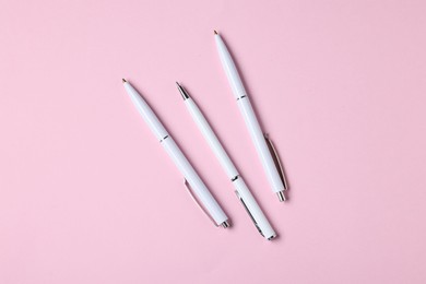 Photo of Ballpoint pens on pink background, flat lay