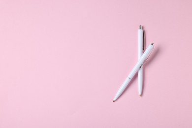 Photo of Ballpoint pens on pink background, top view. Space for text