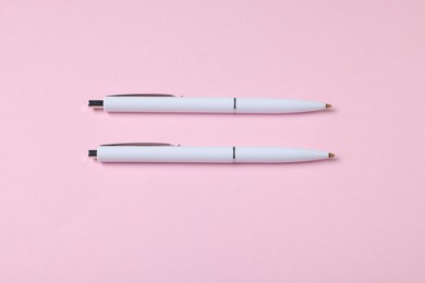 Photo of Ballpoint pens on pink background, flat lay