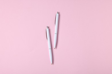 Photo of Ballpoint pens on pink background, flat lay