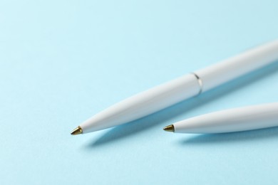 Photo of Stylish pens on light blue background, closeup